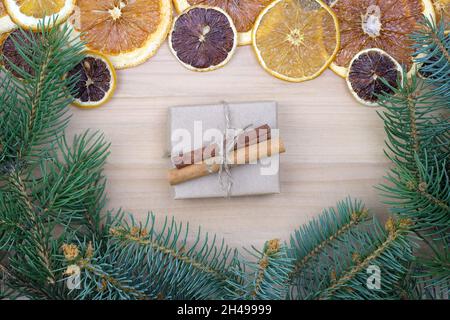 Geschenkschachtel in Bastelpapier mit Zimtstangen verpackt. Weihnachtlicher Hintergrund mit trockenen Orangen, Gewürzen und Zweige eines Weihnachtsbaums. Umweltfreundliches Geschenk Stockfoto