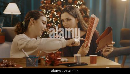 Schwestern bereiten Weihnachtsgeschenke zusammen zu Hause zu, sie wählen das Geschenkpapier Stockfoto