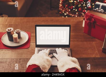 Der Weihnachtsmann verbindet sich mit seinem Laptop und schreibt, leerer Kopierraum, Feiertage und Feiern Stockfoto