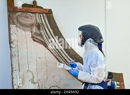 01. November 2021, Brandenburg, Wünsdorf: Ein Restaurator arbeitet in einem Schutzanzug in der Restaurierungswerkstatt des Landesamtes für Denkmalpflege und Archäologisches Landesmuseum (BLDAM) an einem Figurengemälde eines Barocktheaters aus dem Kloster Neuzelle. Dank der großzügigen, langfristigen Unterstützung durch die Beauftragte der Bundesregierung für Kultur und Medien (BKM), die Ostdeutsche Sparkassenstiftung mit der Sparkasse oder-Spree und der Bereitschaft des Bundesministeriums für Wissenschaft, Forschung und Kultur (MWFK), des Landesamtes für Denkmalpflege Brandenburg und der Landesarchäologie-Mus Stockfoto