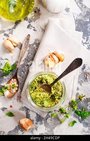 Hausgemachte Petersilie-Pesto-Sauce und Zutaten auf dunklem Zementgrund. Nahaufnahme des Basilikumpesto im Glasgefäß mit Zutaten. Stockfoto