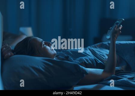 Frau, die nachts im Bett liegt und fernsieht, leidet an Schlaflosigkeit Stockfoto