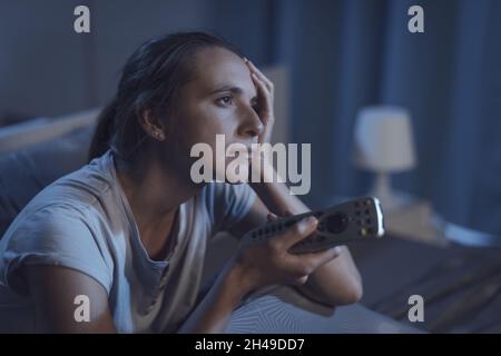 Frau, die nachts im Bett liegt und fernsieht, leidet an Schlaflosigkeit Stockfoto
