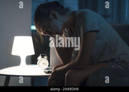 Erschöpfte Frau, die an Schlaflosigkeit leidet, sitzt auf dem Bett und denkt nach Stockfoto