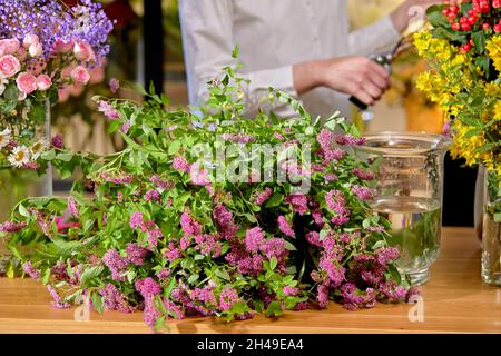 Blumenstrauß aus wilden Frühlingsblumen, der auf dem Tisch liegt, für Blumenstrauß gemacht, Nahaufnahme. Weibliche Floristin im Hintergrund am Arbeitsplatz, die frische Blume arrangiert Stockfoto
