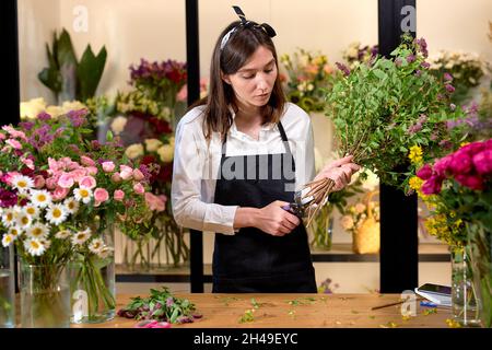 Foto von erfolgreichen modernen Floristen tragen Schürze machen die Schaffung Bouquet von blühenden bunten verschiedenen Blumen in modernen Innenarchitektur floral Shop, mit Stockfoto