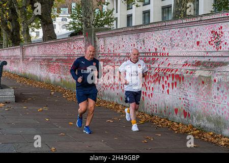 WESTMINSTER LONDON, GROSSBRITANNIEN. November 2021. Jogger laufen entlang der Covid National Memorial Wall am Themse Embankment, da die Zahl der Personen, die Covid in Großbritannien positiv testen, in den letzten Tagen auf mehr als 50,000 Fälle an einem Tag gestiegen ist und Wissenschaftler einen schwierigen Winter befürchten. Die Wand ist ein öffentliches Wandgemälde mit Herzen, das von Freiwilligen gemalt wurde, um den Opfern der COVID-19-Pandemie im Vereinigten Königreich zu gedenken. Kredit: amer ghazzal/Alamy Live Nachrichten Stockfoto