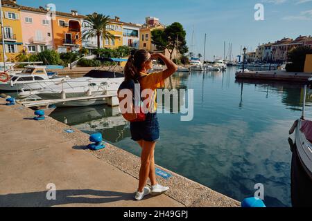 Eine Reisende Frau steht am Pier mit Yachten und Booten am wunderschönen Hafen von Port Saplaya in der Nähe von Valencia mit farbenfrohen Häusern. Reisekonzept Stockfoto