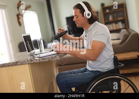 Kaukasischer behinderter Mann, der Podcast mit einem Mikrofon aufnimmt, das zu Hause auf einem Rollstuhl sitzt Stockfoto