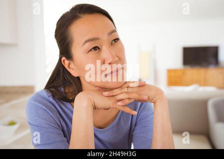 Porträt einer nachdenklichen asiatischen Frau, die zu Hause auf dem Sofa sitzt Stockfoto