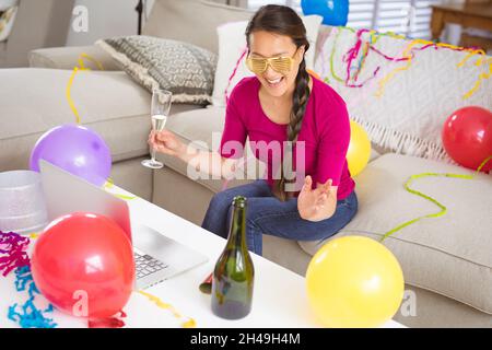 Glückliche asiatische Frau, die ein Sektglas hochhebt und einen Videoanruf für den Laptop am Silvesterabend führt Stockfoto