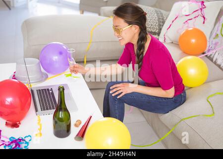 Glückliche asiatische Frau, die ein Sektglas hochhebt und einen Videoanruf für den Laptop am Silvesterabend führt Stockfoto