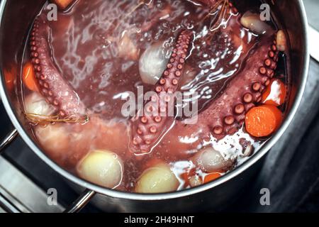 Ganze Oktopus kocht in dem Topf, der mit Wasser und Gemüse gefüllt ist. Tentakeln von rotem Oktopus werden gekocht Stockfoto