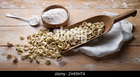 Apulische Vollkornorchiette. Orecchiette pugliesi in Schaufel mit Vollkornweizengrieß auf rustikalem Holzhintergrund, Nahaufnahme. Stockfoto