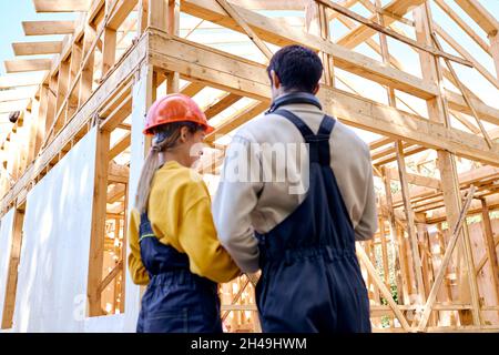 Rückansicht von intelligenten Architekten Konstrukteure halten auf der Baustelle Entwürfe für die Zwischenablage, während sie ihren Arbeitsplan besprechen, Gespräche führen, tragen Stockfoto