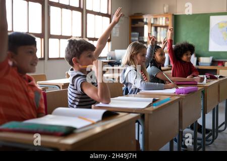 Eine Gruppe von multiethnischen Kindern, die in der Schule auf ihrem Schreibtisch sitzen. Grundschulbildung Stockfoto