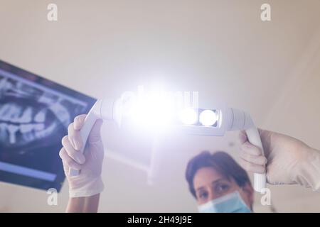 Kaukasische weibliche Zahnkrankenschwester trägt Gesichtsmaske mit Lampe in der modernen Zahnklinik Stockfoto