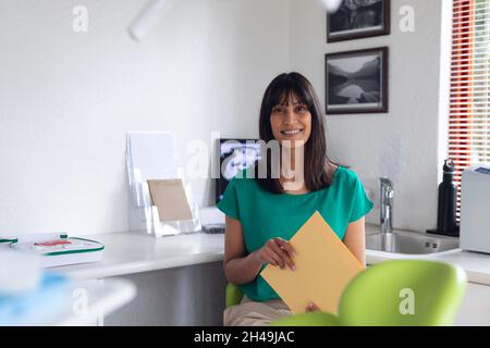 Porträt einer lächelnden biracial weiblichen Patientin, die Dokumente in der modernen Zahnklinik hält Stockfoto