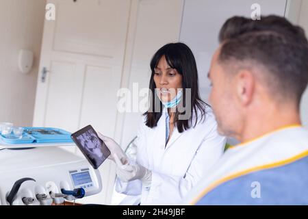 Biracial weibliche Zahnarzt trägt Gesichtsmaske Untersuchung der Zähne von männlichen Patienten in der modernen Zahnklinik Stockfoto