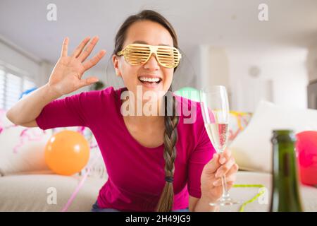 Glückliche asiatische Frau, die ein Sektglas hochhebt und einen Videoanruf für den Laptop am Silvesterabend führt Stockfoto