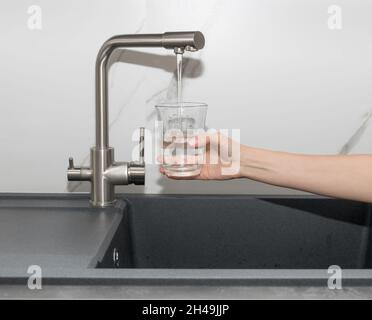 Frau gießt gefiltertes Wasser aus dem Wasserhahn in das Glas in der Küche Stockfoto