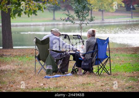 An einem milden Herbsttag bringt ein älteres Paar tragbare Stühle in den Kissena Park und spielt Kartenspiele. In Flushing, Queens, New York City Stockfoto