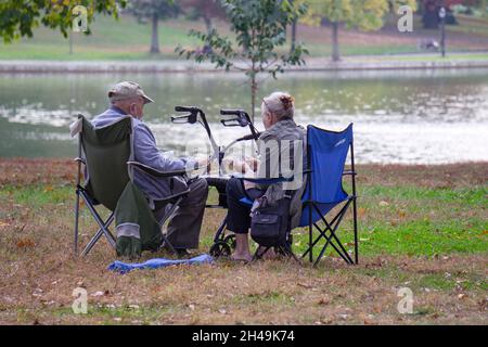 An einem milden Herbsttag bringt ein älteres Paar tragbare Stühle in den Kissena Park und spielt Kartenspiele. In Flushing, Queens, New York City Stockfoto