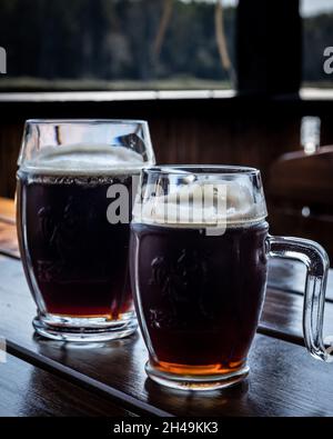 Dziwnow, Polen - 10. September 2021: Zwei Glasbecher, gefüllt mit dunklem Bier, stehen auf dem Tisch. Stockfoto