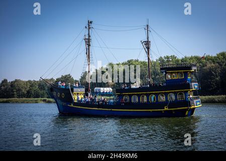 Dziwnow, Polen - 10. September 2021: Ein blau-gelbes Touristenboot, das auf dem Dziwna-Kanal segelt. Stockfoto