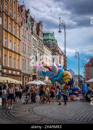 Breslau, Polen - 7. August 2021: Leute, die am sonnigen Sommertag auf dem Marktplatz der Altstadt spazieren gehen. Bunte Ballons. Wunderschöne Wohnhäuser. Stockfoto