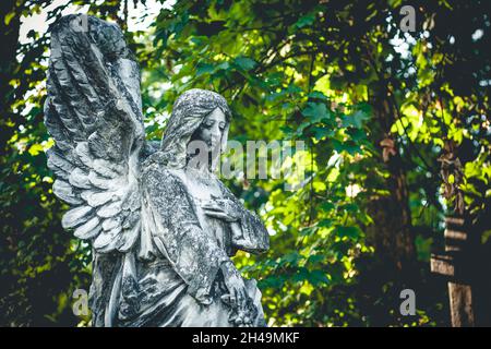 Skulptur des Engels auf dem Friedhof mit grünen Blättern im Hintergrund Stockfoto