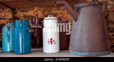 Blaue, braune und weiße Milchbehälter im Retro-Look stehen auf einem Holzregal. Stockfoto