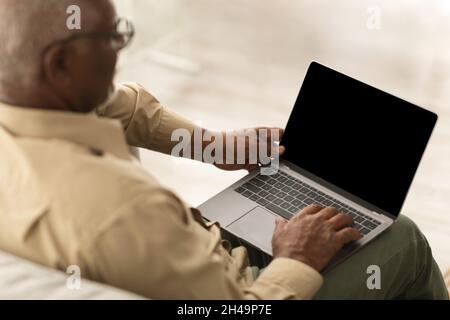 Rückansicht Von Senior Black Man Mit Laptop Mit Leerem Computer-Bildschirm Für Website-Werbung Sitzen Arbeiten Online Innen. High-Angle-Ansicht. Mocku Stockfoto