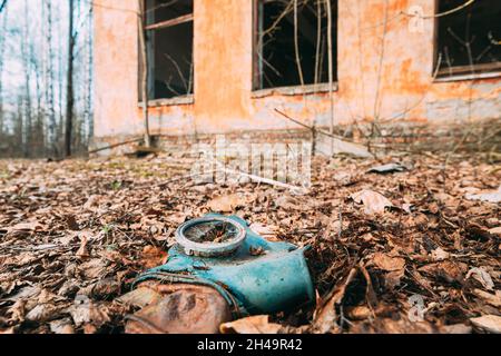 Gasmaske In Der Nähe Des Verlassenen Zerstörten Schulgebäudes Des Alten Dorfes In Der Umsiedlungszone Von Tschernobyl. Weißrussland. Katastrophe Von Tschornobyl. Heruntergekommenes Haus Stockfoto