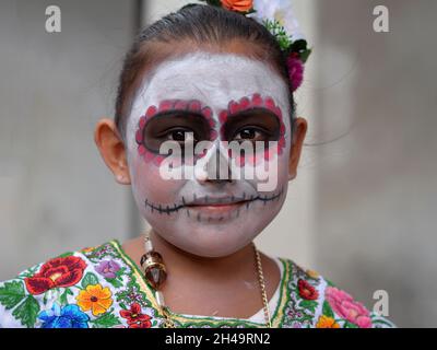 Mexikanisches Yucatecan kleines Mädchen mit traditionellem gemaltem Gesicht Make-up (calavera) am Tag der Toten (Dia de los Muertos) schaut auf den Betrachter. Stockfoto