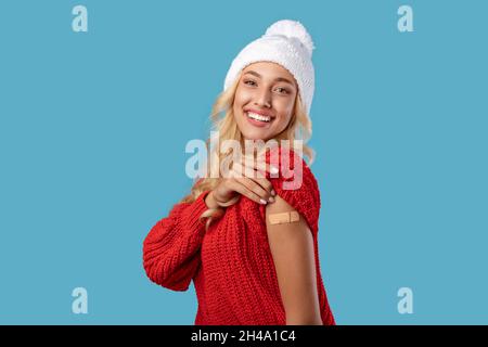 Werbung Für Die Impfung Gegen Coronaviren. Glückliche geimpfte Frau in weißem Winterhut zeigt Arm mit klebenden Gips nach Covid-19-Impfstoffeinspritzung P Stockfoto