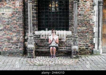 Verspielte Touristen sitzen als Gebet auf einer alten Bank, Brügge, Belgien Stockfoto