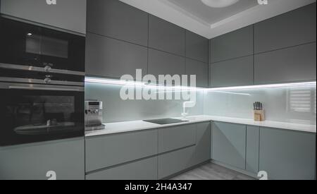Moderne voll ausgestattete Küche mit Küchengeräten in grau und weiß. Schönes LED-Licht Stockfoto