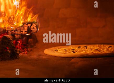 Pizza in der Nähe des Feuers im Ofen, der in Flammen brennt Stockfoto