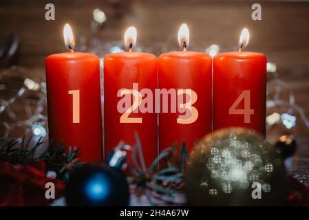 Vier nummerierte rote Adventskerzen mit drei Kerzen angezündet und als Vorlage im Schnee liegende Weihnachtsdekoration Stockfoto