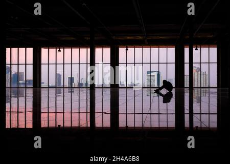 Müder oder depressiver Geschäftsmann, der auf dem Boden sitzt und die Hände allein am Kopf im leeren Raum des hohen Bürogebäudes hält. Stockfoto