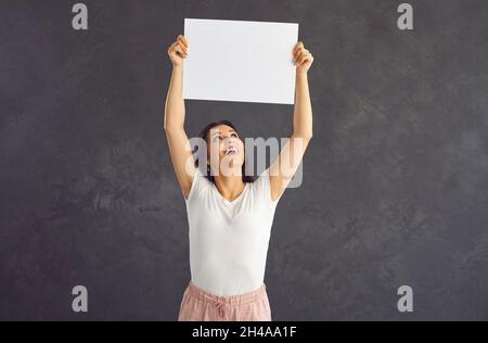 Junge schöne Frau über ihrem Kopf mit leerem weißen Blatt Papier, das auf grauem Hintergrund steht. Stockfoto