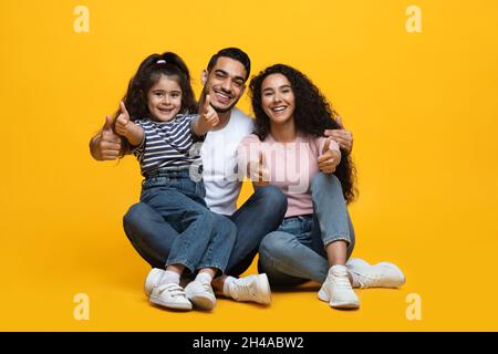 Wir Können Es Empfehlen. Porträt Einer Glücklichen Arabischen Familie Von Drei Zeigt Daumen Nach Oben An Der Kamera, Fröhliche Eltern Aus Dem Nahen Osten Und Kleine Tochter, Die Zeichen Von Gestikuliert Stockfoto