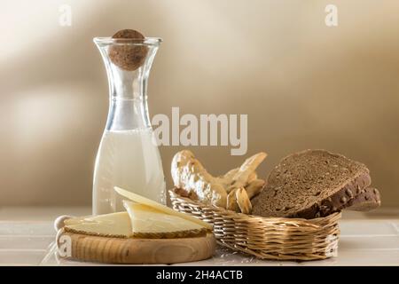 Milchflasche und Korbkorb mit verschiedenen Brötchen, Roggenbrot und Rohrdonuts. Tisch mit Käse Stockfoto