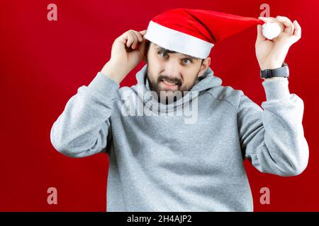 Fröhlicher bärtiger Mann, der einen roten Hut des Weihnachtsmannes aufsetzt. Stockfoto
