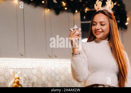 Ein Mädchen zu Weihnachten hält einen Keks in ihren Händen und lächelt.Frau am Silvesterabend in der Küche Stockfoto