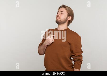 Porträt eines stolzen arroganten Mannes mit Bart, der ein Sweatshirt trägt, egoistisch mit dem Finger auf sich zeigt und seine Verdienste rühmt und bewundert. Innenaufnahme des Studios isoliert auf grauem Hintergrund. Stockfoto