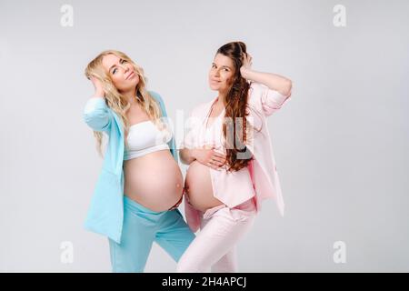 Zwei Schwangere mit großen Bäuchen in Anzügen auf grauem Hintergrund. Stockfoto