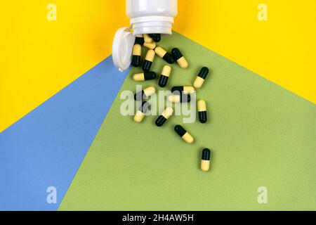 Medizinische Pillen aus einem weißen Glas auf einem bunten Hintergrund verstreut. Color 2021 Konzept. Kosmetologie und Medizin Konzept. Kräuterkapseln. Stockfoto