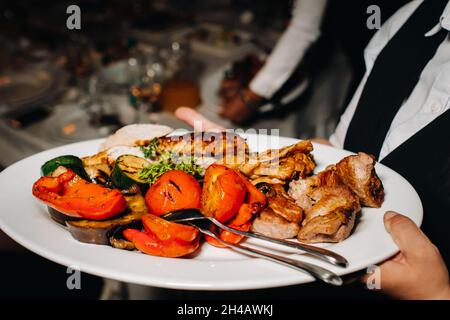Am Abend serviert das Restaurant in einem Restaurant ein warmes Grillgericht mit vegetables.fried Fleisch mit Tomaten und anderem Gemüse auf einem Teller Stockfoto